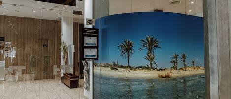 A modern interior with a 'CAFETERIA RESTAURANTE' sign, a beach mural, and a 'PROGRAMACION DEPORTIVA' sign.