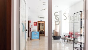 A modern interior with a reception desk, a seating area with chairs, and a glass partition with a logo. - Hotel Traíña (San Pedro del Pinatar)