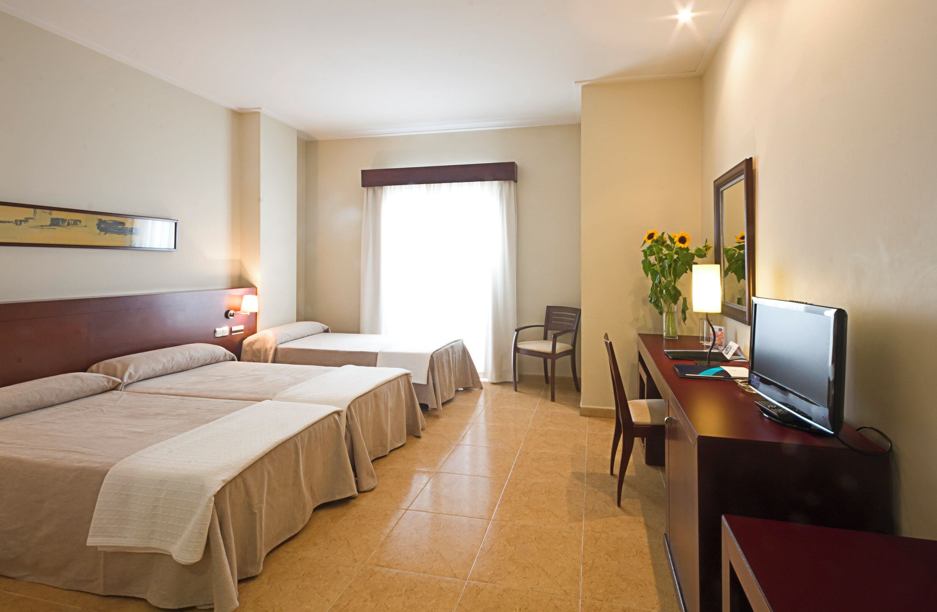 A hotel room with two beds, a desk with a computer, a chair, a TV, and a window with curtains.
