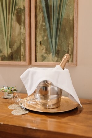 A champagne bottle on a silver bucket with a white cloth cover, placed on a wooden table with a placemat. - Hotel Traíña (San Pedro del Pinatar)