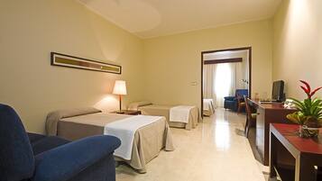 A hotel room with two beds, a desk, a chair, a TV, and a potted plant.