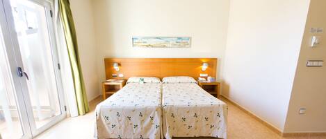 Uma cama de casal com cabeceira de madeira, duas mesas de cabeceira com luminárias, um quadro na parede e uma porta de vidro deslizante com cortinas.