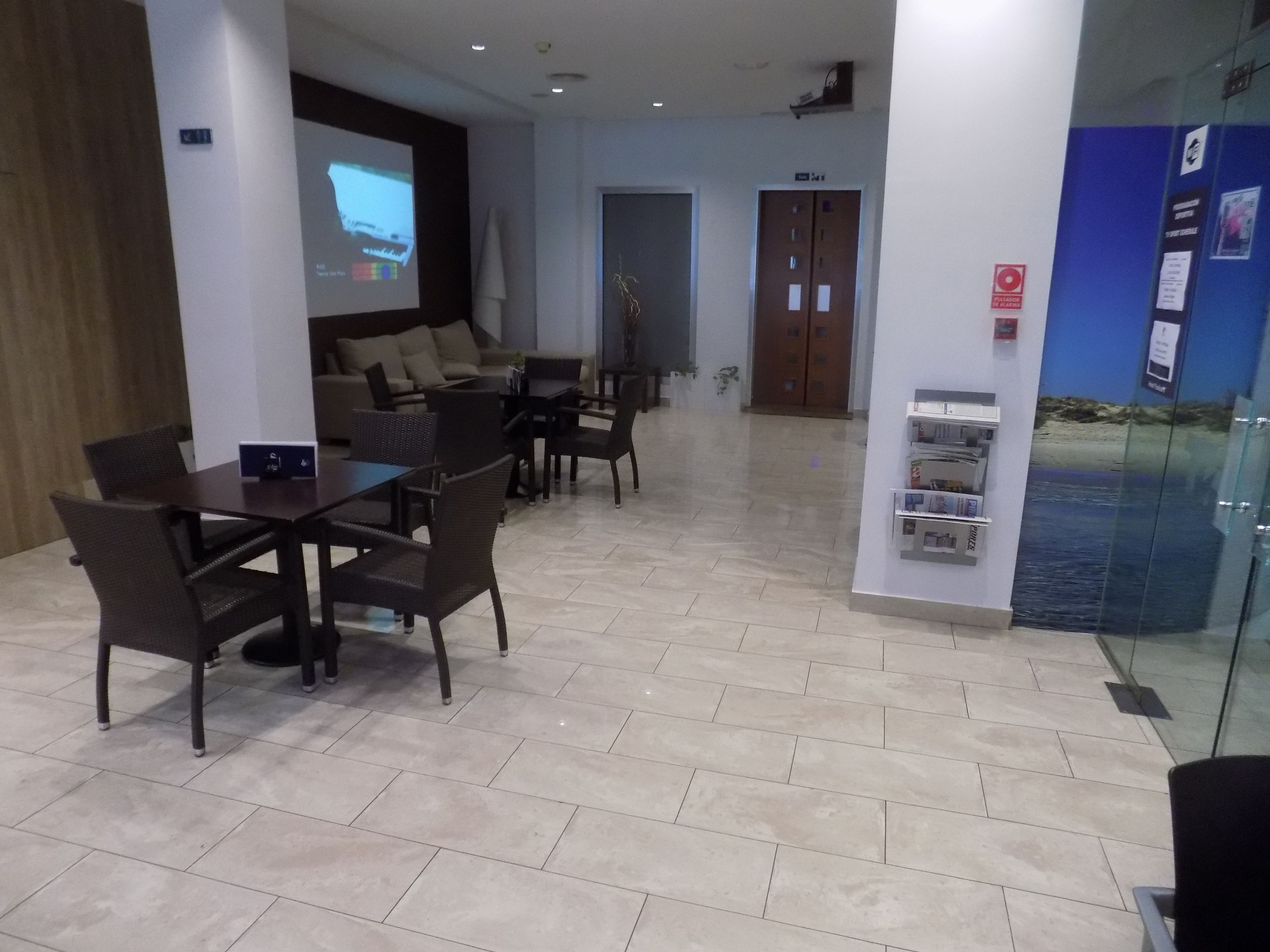 Una sala de conferencias moderna con una pantalla grande, asientos cómodos y una zona de recepción con pared de vidrio.