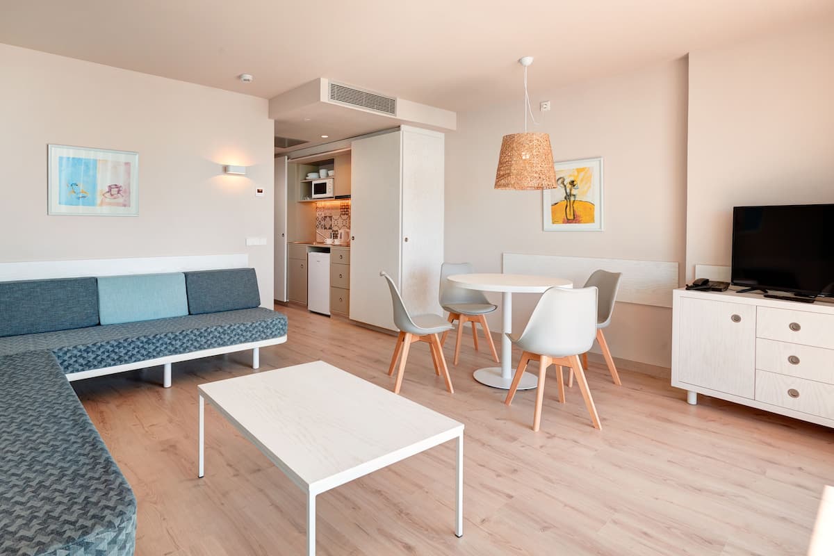 A modern living room with a sofa, a dining table with chairs, a TV, and a kitchen area in the background.
