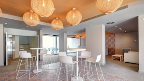 A modern interior with a dining area featuring white chairs and tables, a patterned floor, and hanging wicker lamps. - Protur Atalaya Apartamentos (Son Servera)