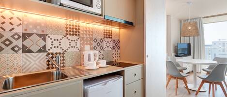 Una cocina moderna con microondas integrado, un lavamanos y un refrigerador pequeño. Hay una zona de comedor con una mesa redonda y sillas.