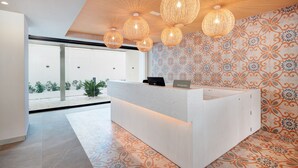 A reception desk with a modern design, surrounded by patterned wallpaper and a large window offering a view of the outdoors. - Protur Atalaya Apartamentos (Son Servera)