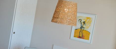 A dining area with a round table and four chairs, a woven pendant light, and a framed artwork on the wall.