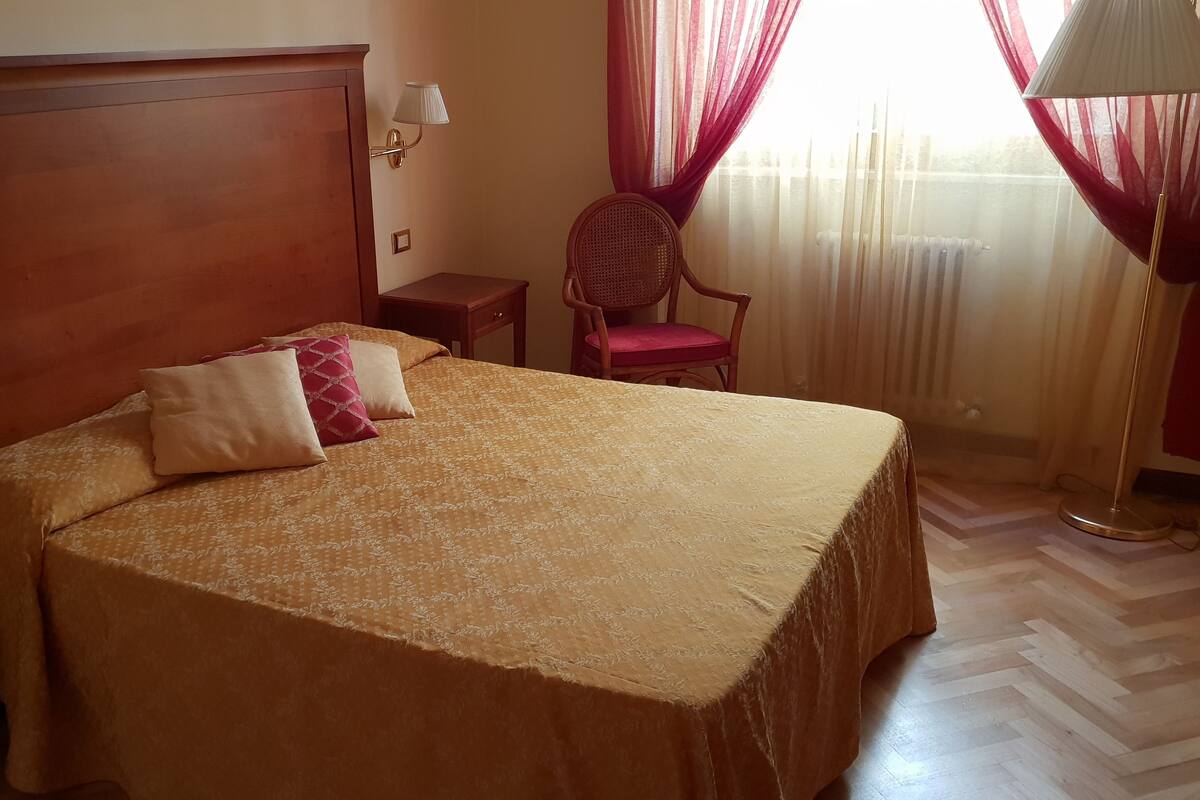 A hotel room with a large bed, a wooden headboard, a bedside table, a chair, and a floor lamp.
