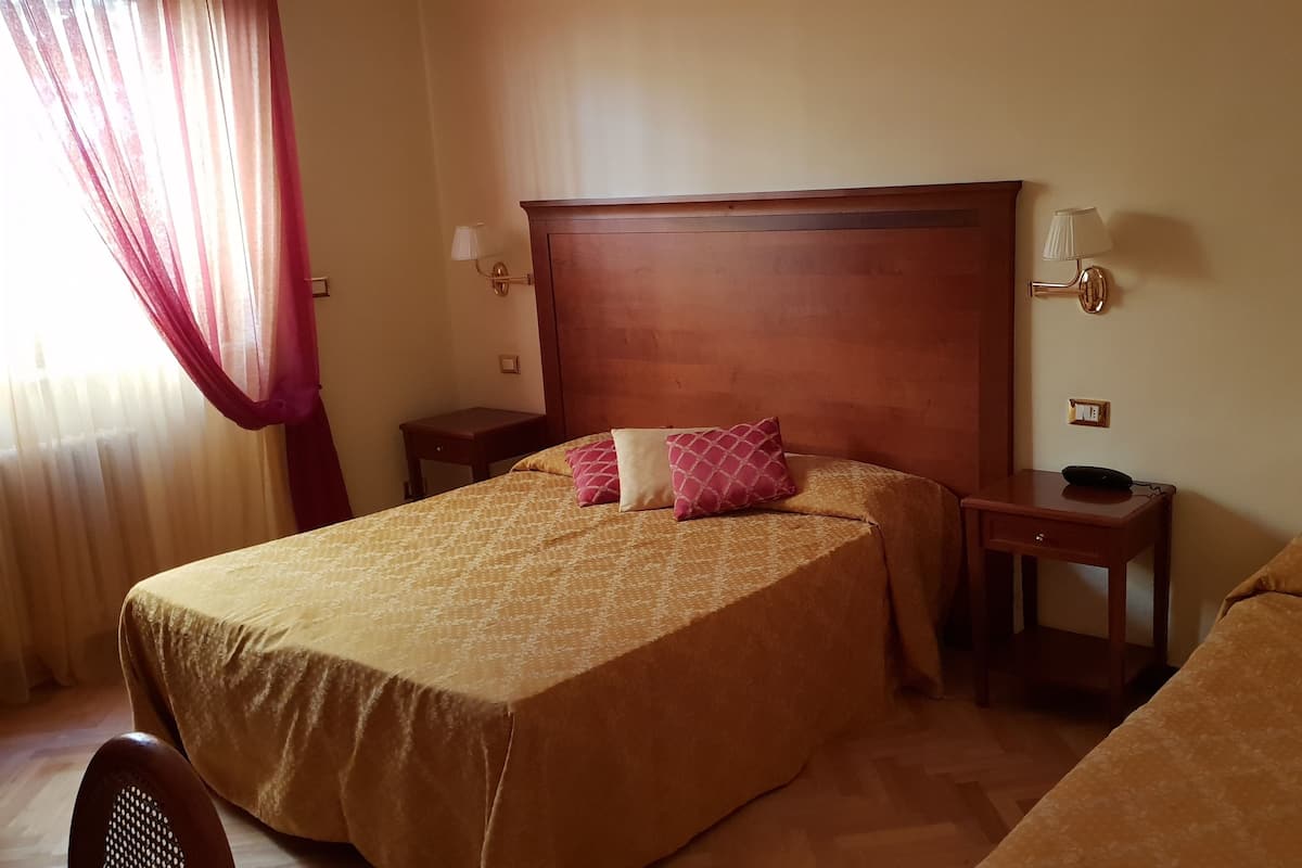A hotel room with two beds, a wooden headboard, bedside tables, lamps, and a small desk with a phone.