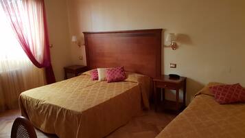 A hotel room with two beds, a wooden headboard, bedside tables, lamps, and a small desk with a phone.