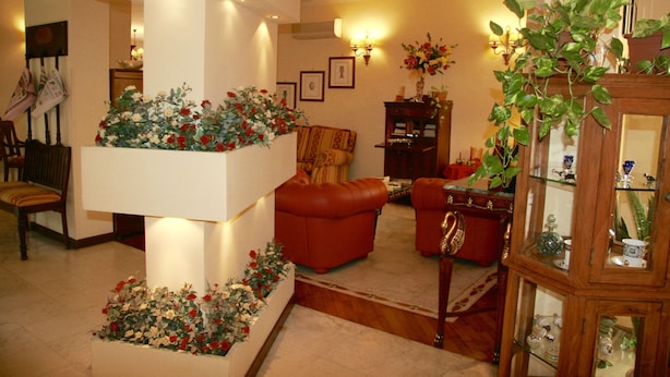 Un vestíbulo con una columna central, un sofá de cuero rojo, un armario de madera con puertas de cristal y una escalera.