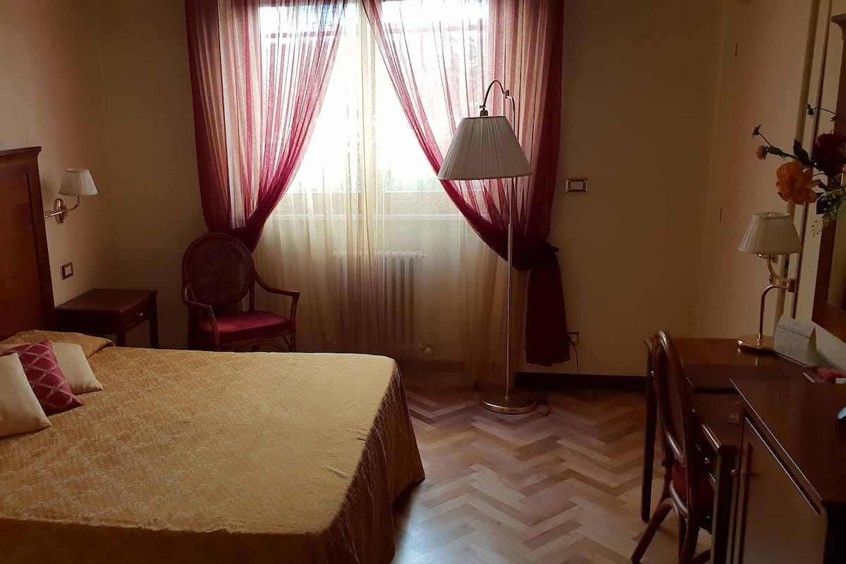 A hotel room with a large bed, a chair, a desk, and a lamp.