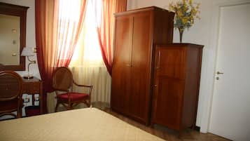 A bedroom with a bed, a wooden wardrobe, a chair, a desk, and a lamp.