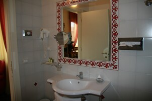 A bathroom with a white sink, a mirror with a decorative frame, a hairdryer, and a towel rack.