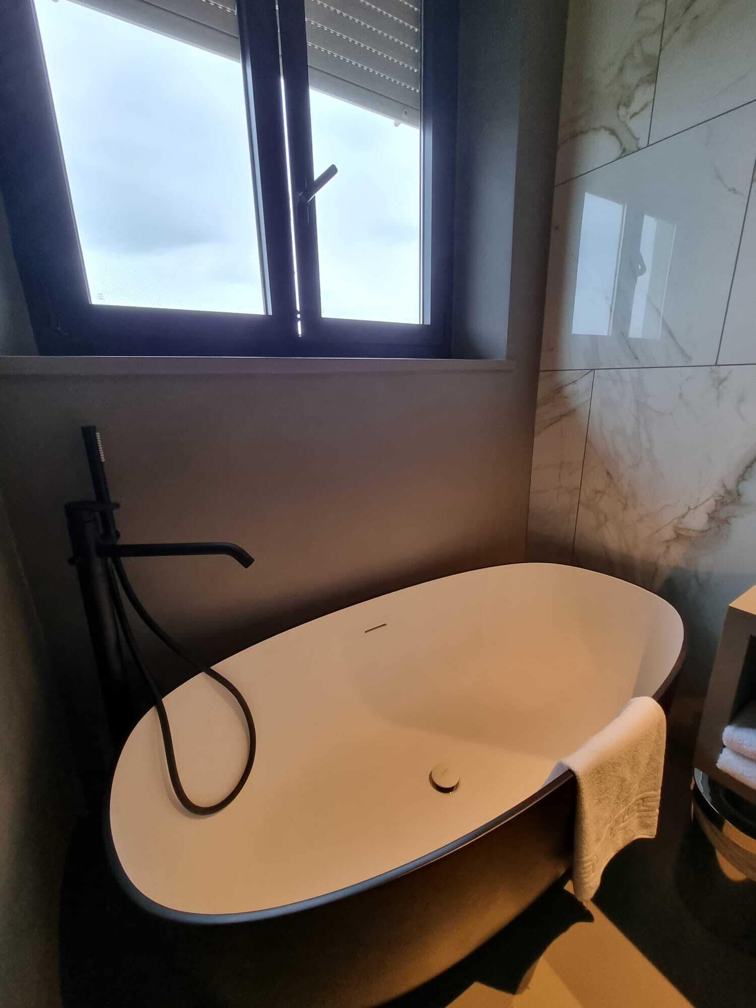Une salle de bain moderne avec une baignoire sur pieds, une fenêtre et des murs en marbre.