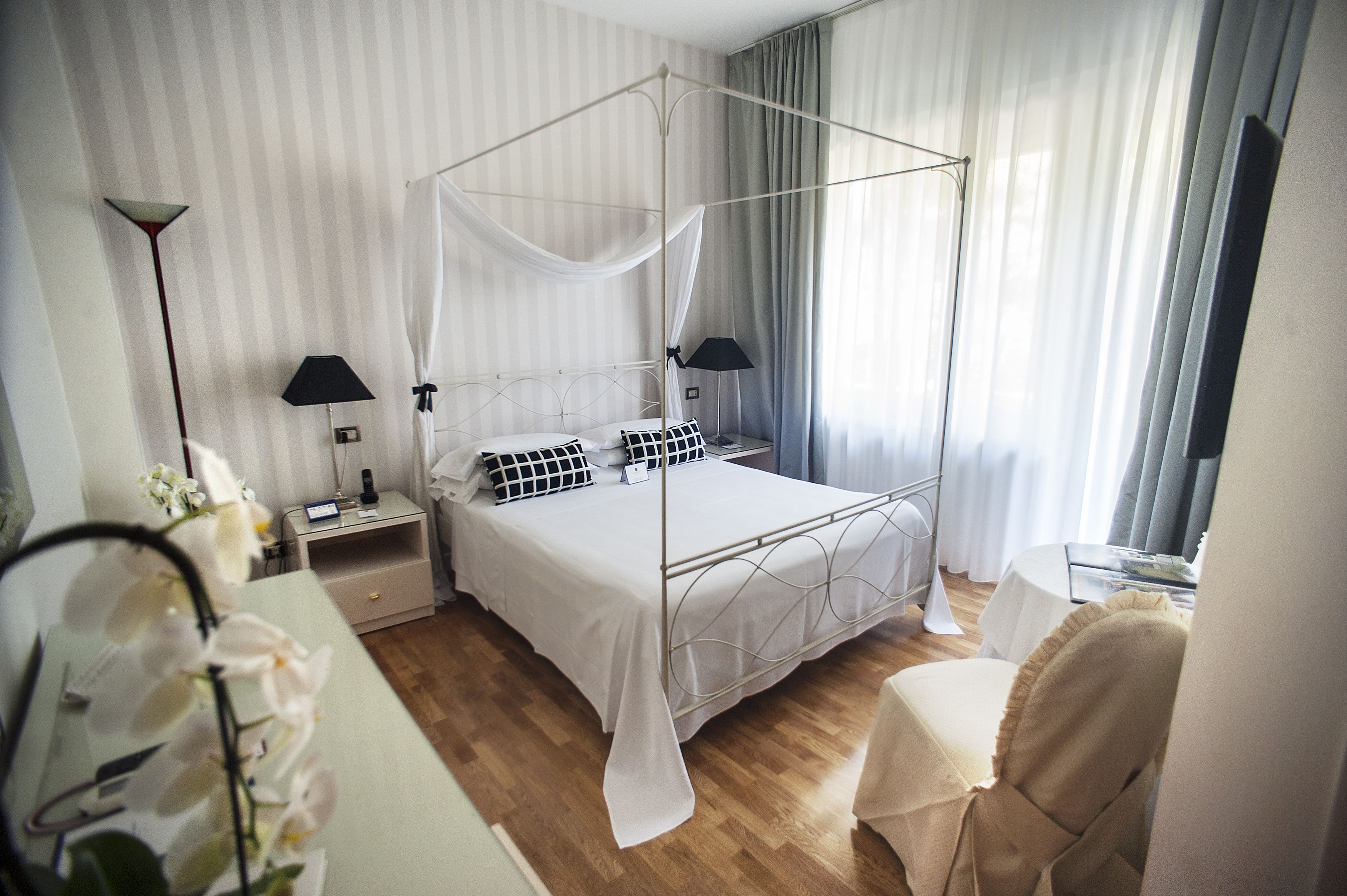 A neatly arranged bedroom with a four-poster bed, bedside lamps, a nightstand, and a chair.