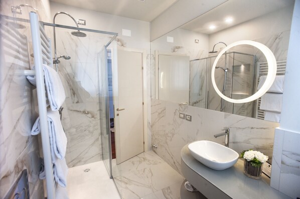 Une salle de bain moderne avec une douche à parois de verre, un lavabo blanc et un sol carrelé en marbre.