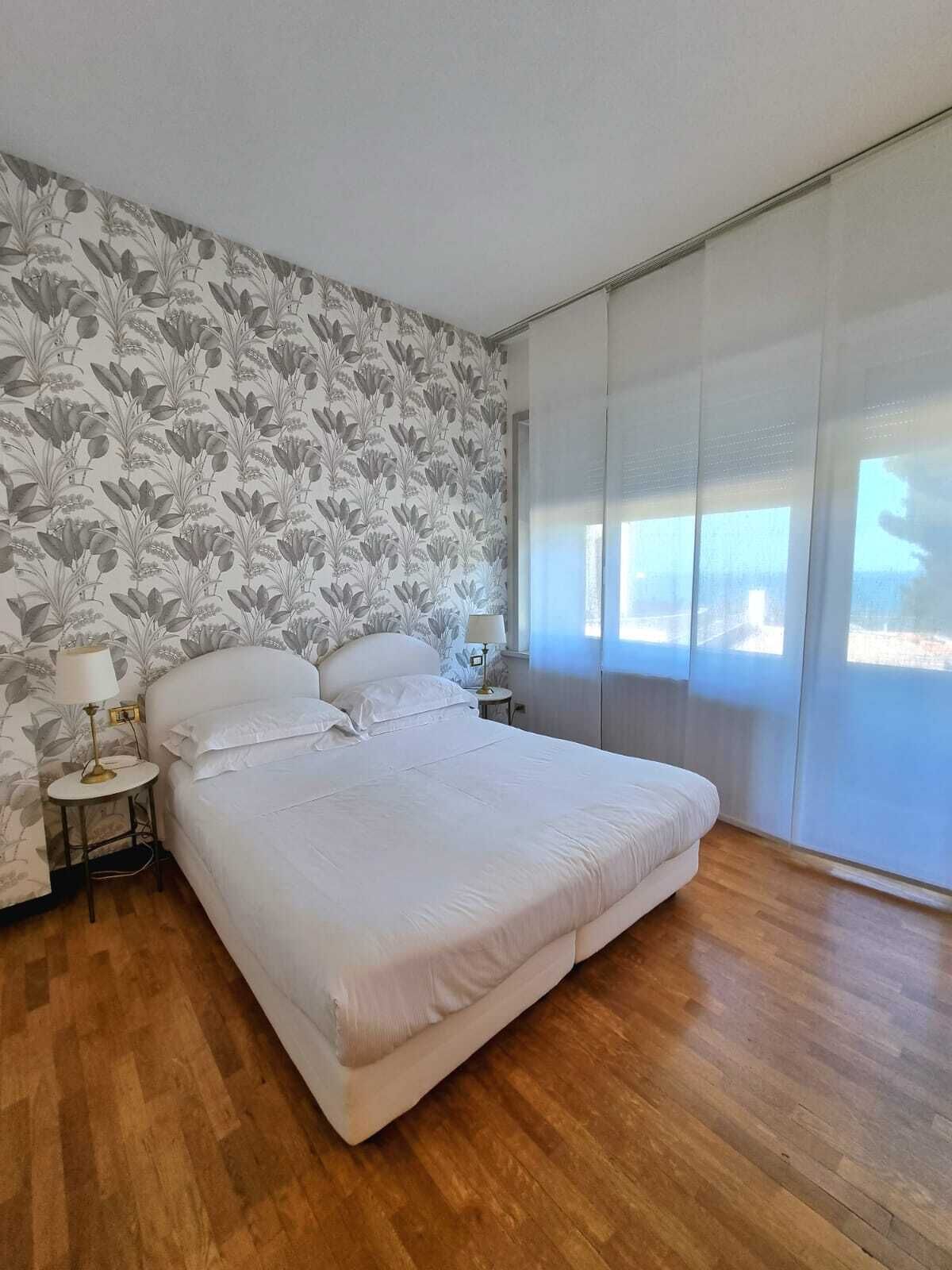 A bedroom with a large bed, a nightstand, a lamp, and a window with a view.