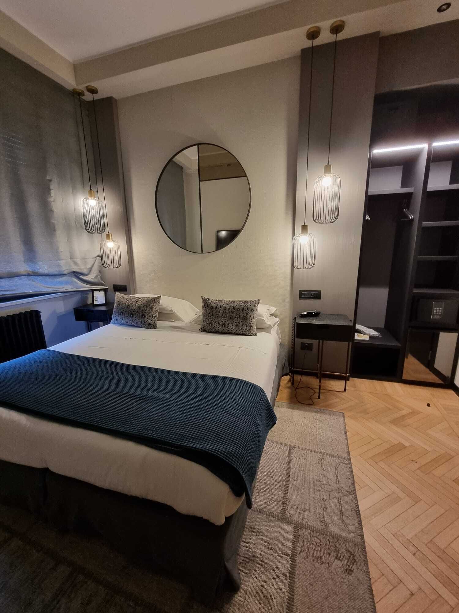 Et moderne soveværelse med en stor seng, et rundt spejl, hængende lamper og en indbygget garderobe.