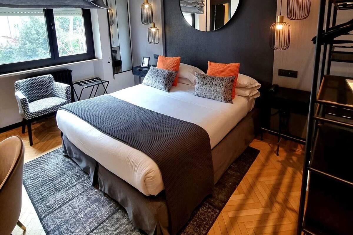 A modern bedroom with a large bed, a round mirror, and a view of the outdoors.