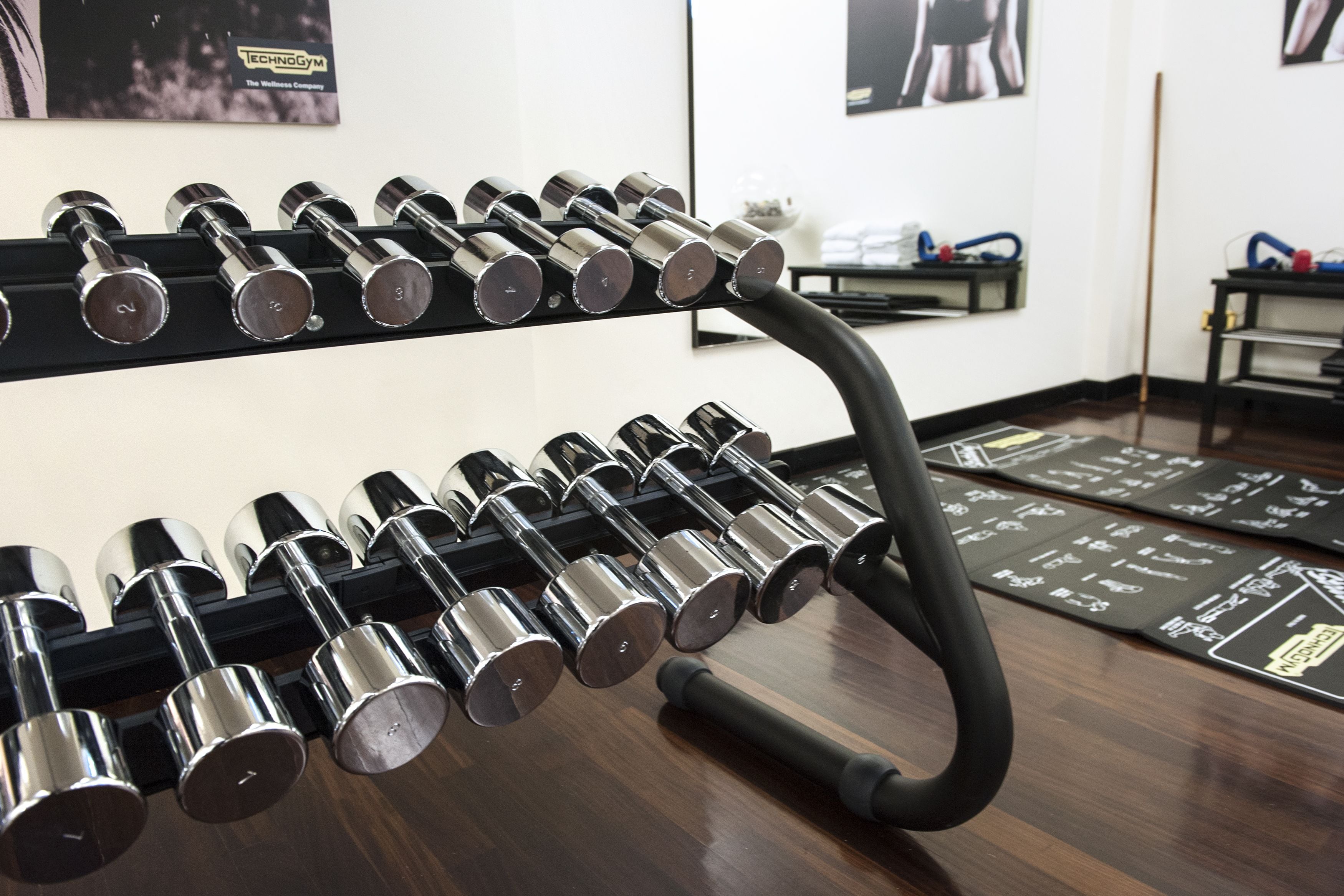 Un gimnasio con un estante de mancuernas y una colchoneta negra en el suelo.