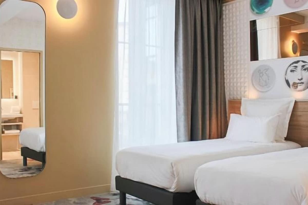 Hotellihuone, jossa on kaksi sänkyä, suuri peili ja taideteoksia seinällä.