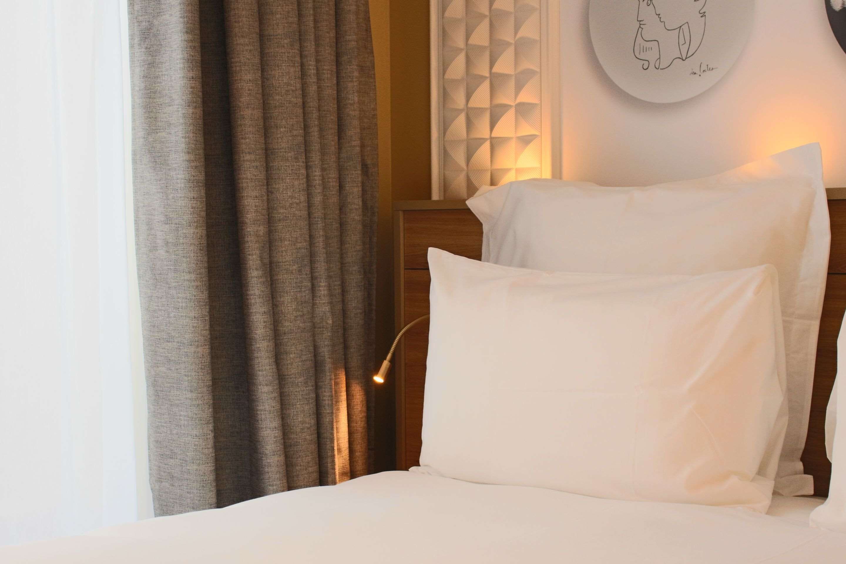 A neatly made bed with white linens, a bedside lamp, and a wall with a geometric patterned design.