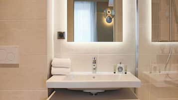 A modern bathroom with a white sink, a mirror above it, and a shower to the right.