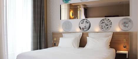 A hotel room with a bed, a bedside table, a mirror, and wall-mounted artwork.