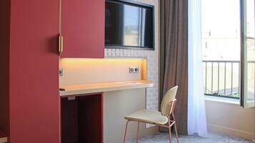 A room with a TV mounted on the wall, a desk with a chair, and a window with curtains.