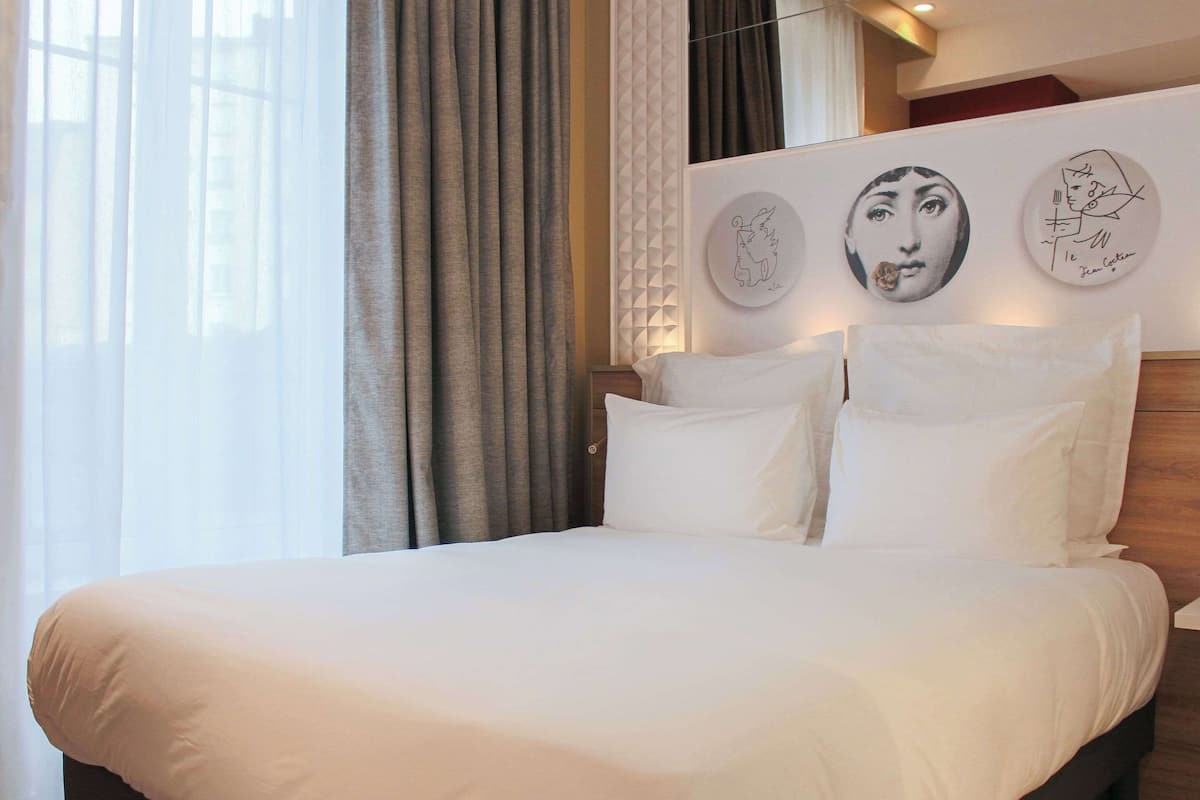 Une chambre d’hôtel avec un grand lit, une fenêtre avec des rideaux et des œuvres d’art murales.