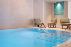Una piscina con superficie de agua azul cristalina, rodeada de sillas de madera y una pequeña mesa.