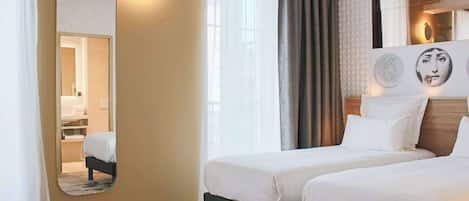A hotel room with two beds, a large mirror, a window with curtains, and wall art.