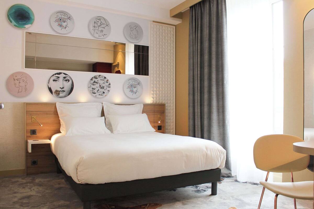 Une chambre d’hôtel moderne avec un grand lit, des tables de chevet, une petite table et une chaise.