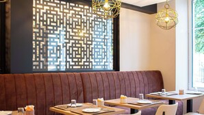 Interior de restaurante con un banco acolchado marrón, mesas y sillas de madera.