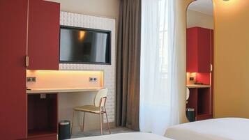 Una camera d'hotel con un letto, una scrivania con una sedia, una televisione e uno specchio.