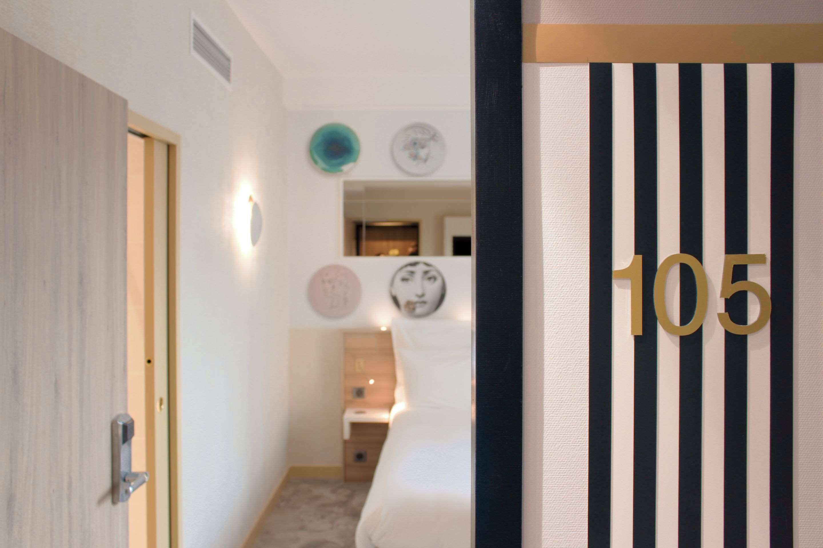 Une chambre d’hôtel avec un lit, une porte et un mur portant le numéro 105.