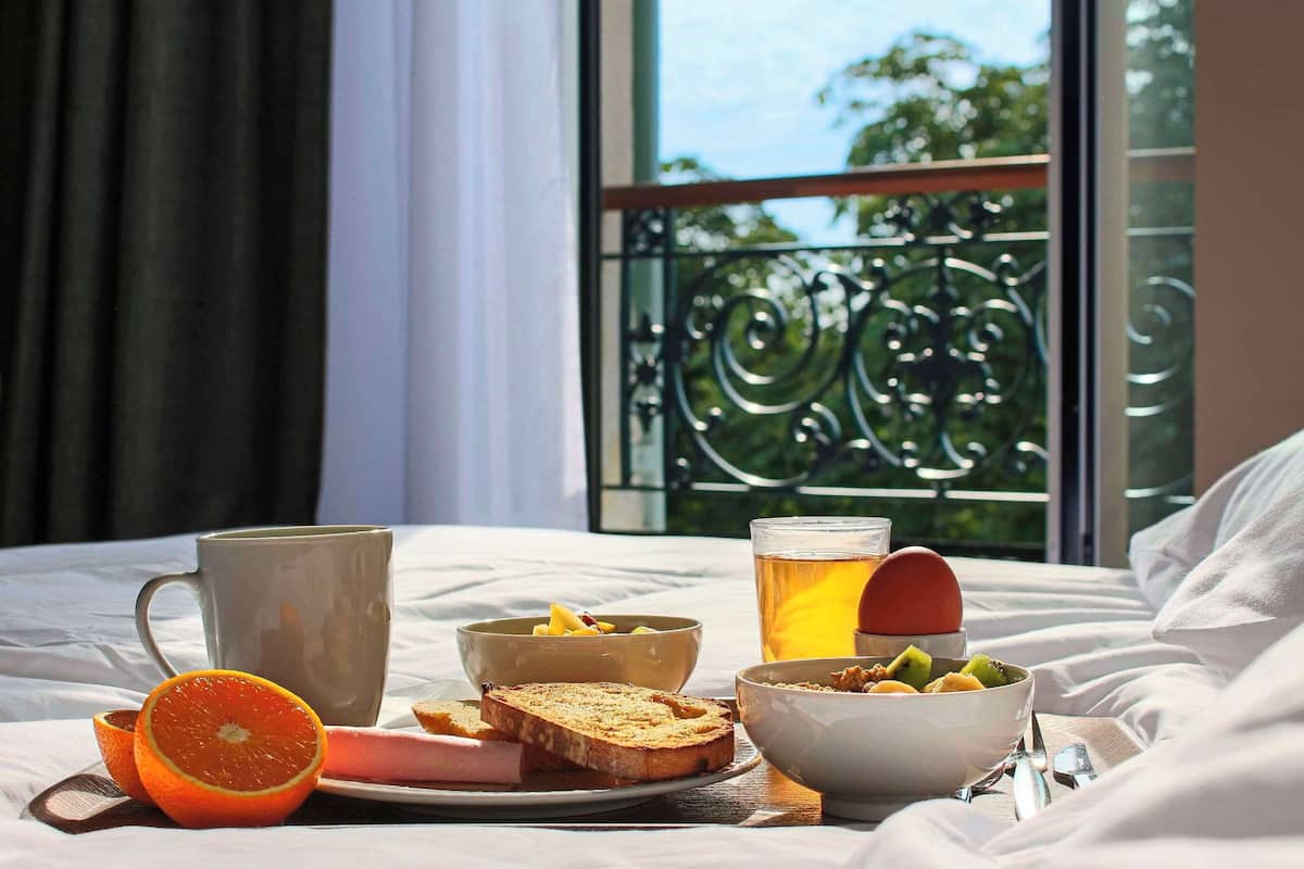 Un plateau de petit-déjeuner installé sur un lit, avec vue sur un balcon.