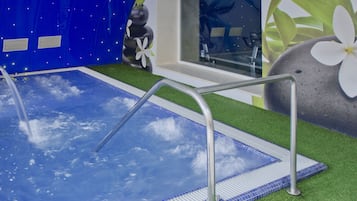 A swimming pool with a glass bottom, surrounded by artificial grass and a stone feature with a white flower.