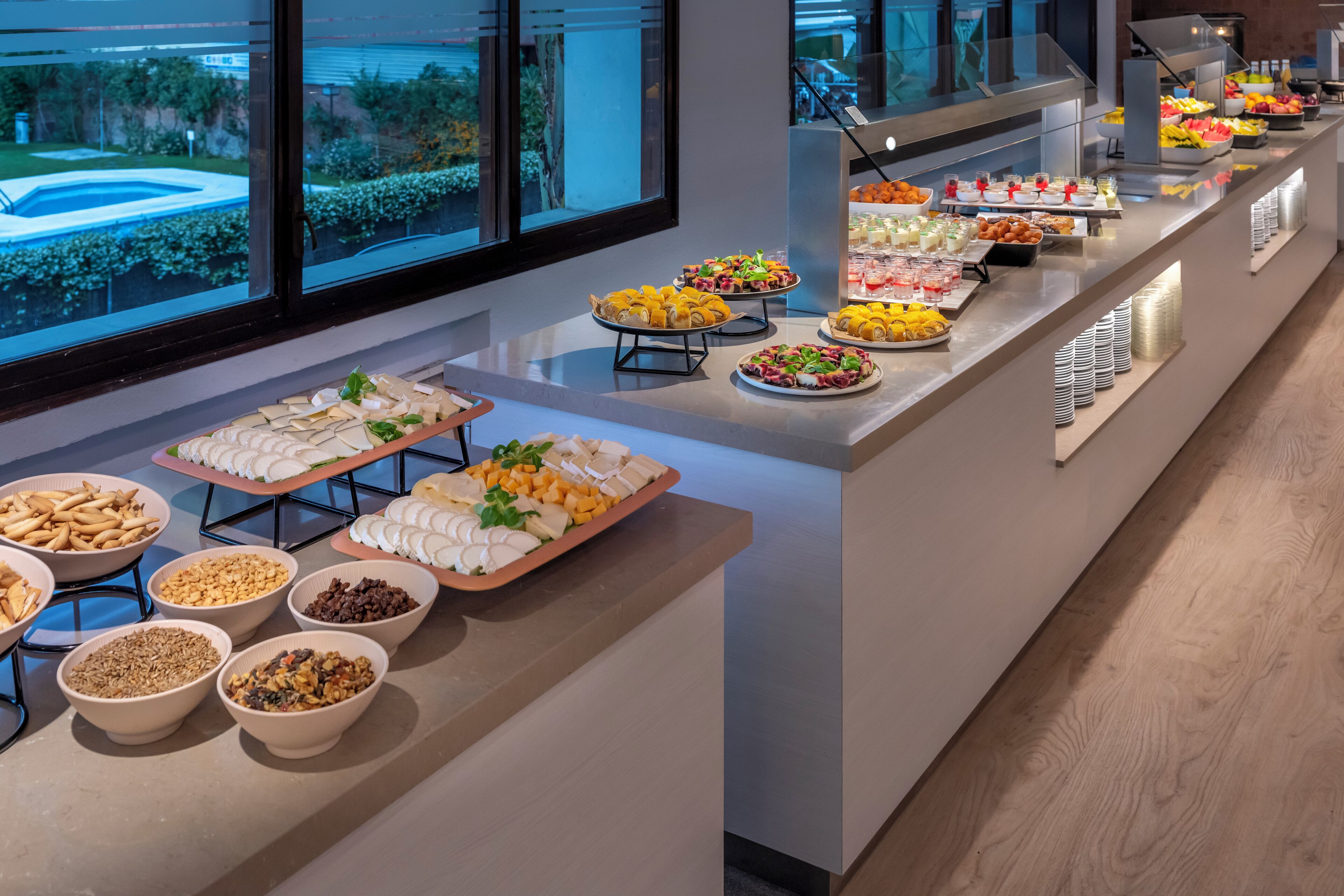 A buffet with various food items and a pool view in the background.