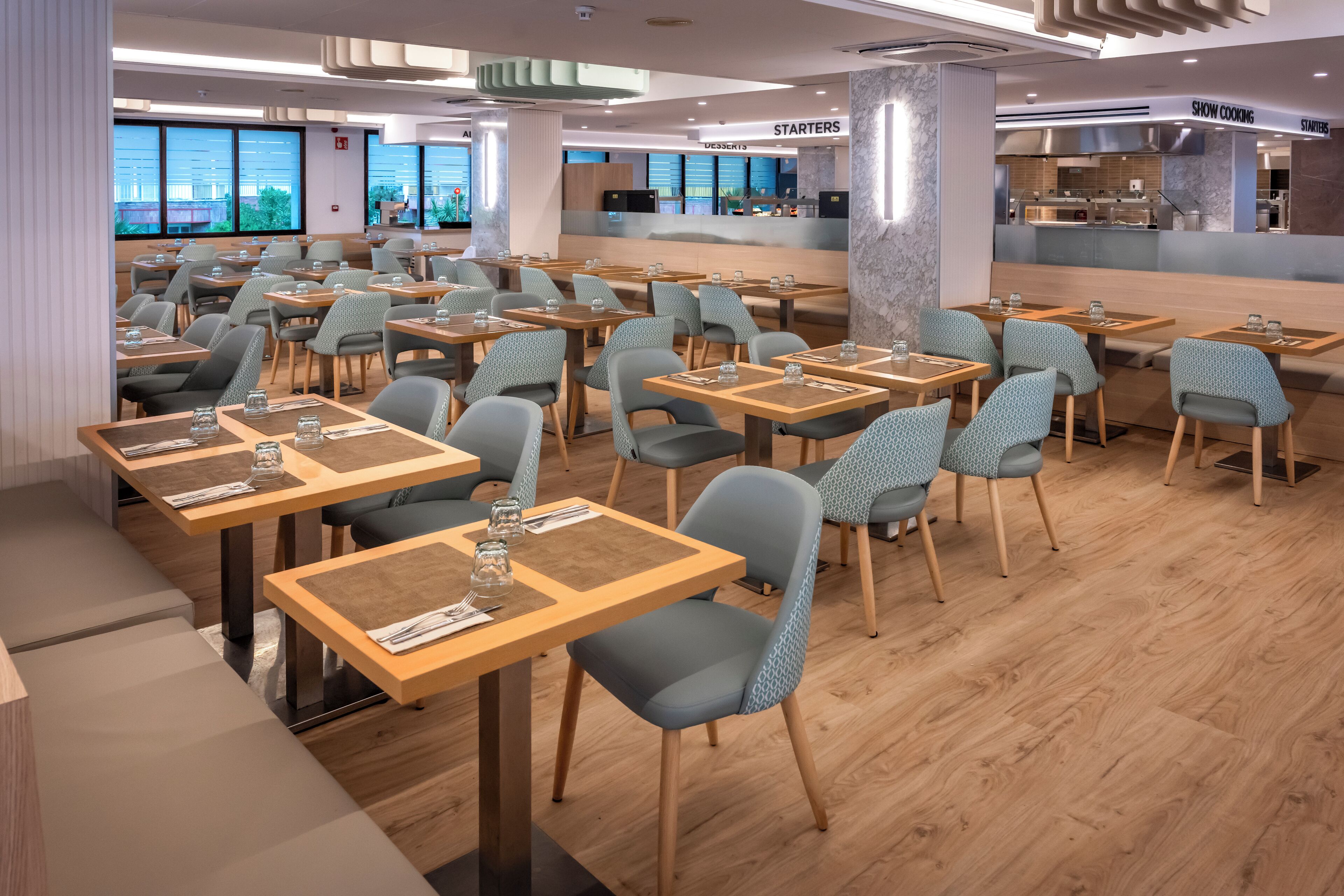 Un restaurante moderno con varias mesas y sillas, una barra con un menú y vistas a la ciudad a través de amplios ventanales.