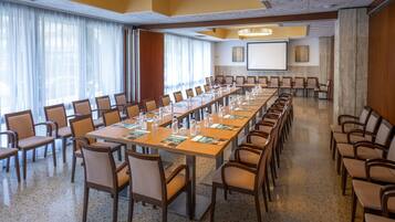 Un salón de conferencias con una larga mesa, sillas y una pantalla de proyector.
