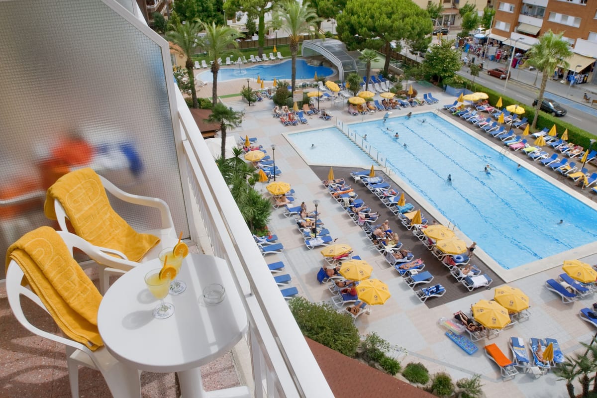 Varanda de hotel com área de piscina, incluindo várias piscinas, espreguiçadeiras e guarda-sóis.