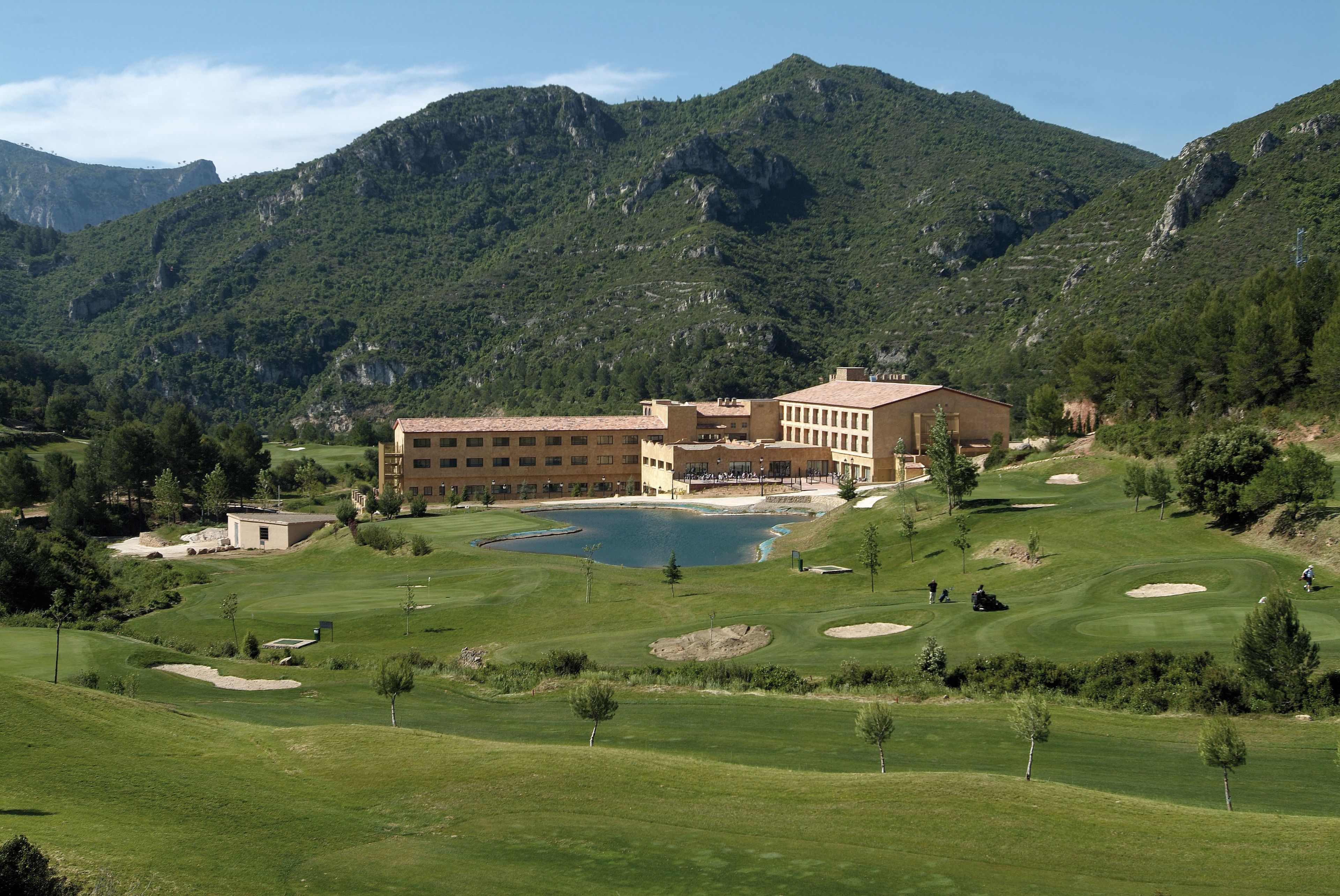 Un terrain de golf avec un grand bâtiment en arrière-plan, entouré de montagnes.