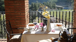 A balcony with a table set for breakfast, including croissants, a glass of red wine, and a vase with flowers. - La Figuerola Hotel & Restaurant (Vandellos i l'Hospitalet de l'Infant)