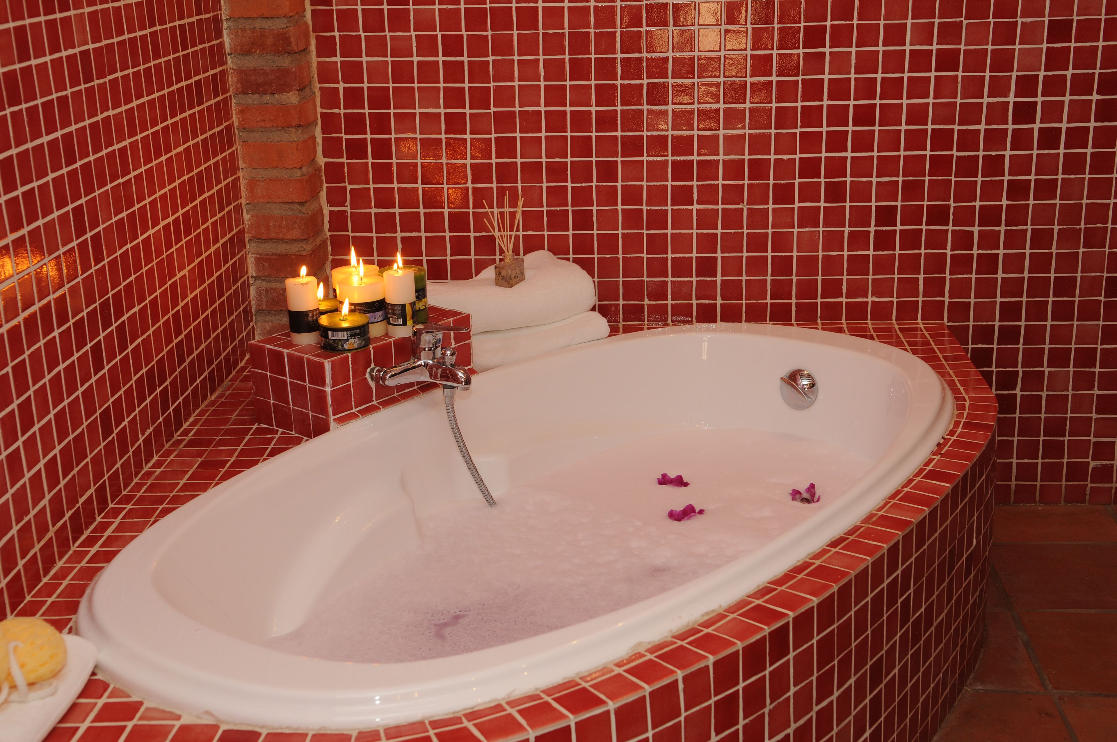 A bathroom with a freestanding bathtub, red-tiled walls, and candles on a shelf.