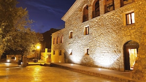 A stone building with arched windows and balconies, illuminated by warm lighting. - La Figuerola Hotel & Restaurant (Vandellos i l'Hospitalet de l'Infant)