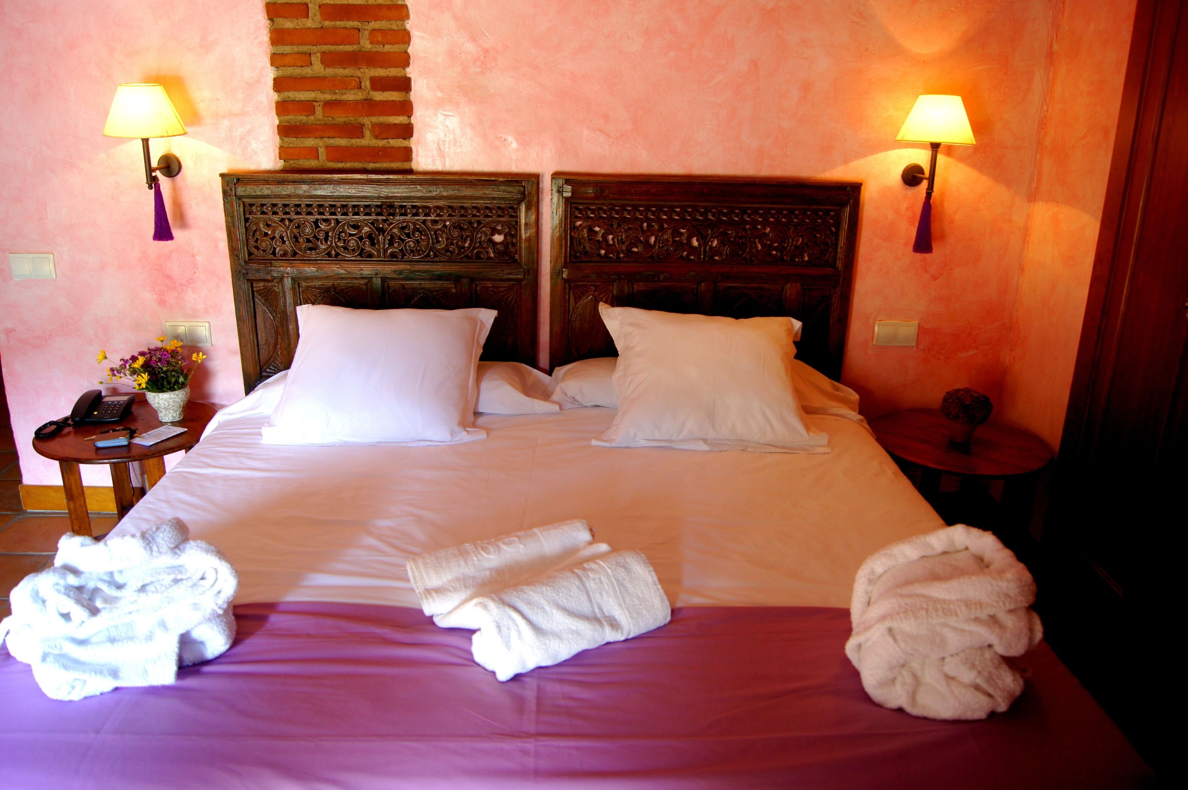 A hotel room with a large bed, two bedside lamps, a small table with a lamp, and a vase with flowers.