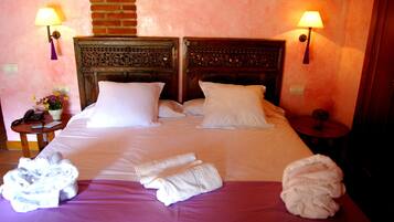 A hotel room with a large bed, two bedside lamps, a small table with a lamp, and a vase with flowers.